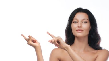 Uzun siyah saçlı, kendine güvenen bir kadın beyaz arka planda her iki tarafı da işaret ediyor. Reklamlar için ideal, promosyon içeriği, ve güzellik veya cilt kampanyaları için geniş kopya alanı ile. 