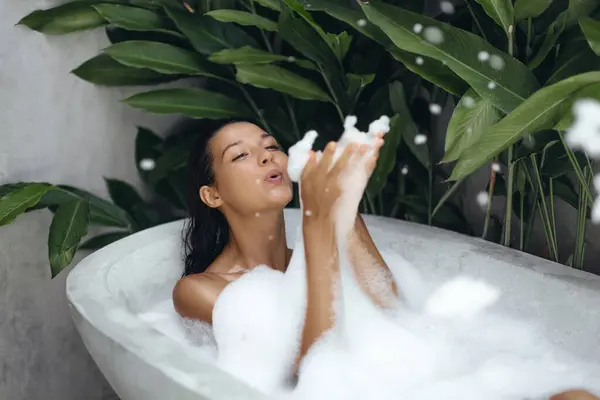 stock image A beautiful woman enjoys a playful bubble bath in a tropical outdoor setting, surrounded by lush greenery. Ideal for concepts of relaxation, luxury, and spa lifestyle in advertisements and promotional