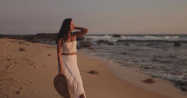 Sri Lanka 'da gün batımında plajda yürüyen beyaz giysili zarif bir kadın ağır çekimde yakalandı. Seyahat, moda ve yaşam tarzı temalı yüksek kaliteli promosyonlar ve reklamlar için mükemmel..