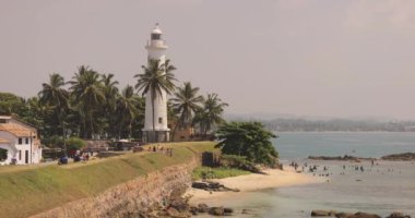 Galle Kalesi deniz feneri, Sri Lanka 'da manzaralı bir plaja ve palmiye ağaçlarına tepeden bakan yükseklerdedir. Bu yüksek kaliteli görüntü, seyahat blogları ve turizm için mükemmel olan tarihi cazibeyi ve tropikal güzelliği yakalıyor.