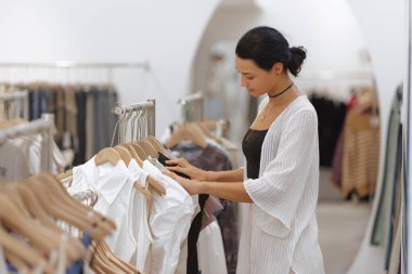 Moda mağazasında kıyafet seçen ve gezinen bir kadın. Sahne, alışveriş deneyimini, stili ve moda eğilimlerini yakalıyor. Perakende, moda ve yaşam tarzı için mükemmel.