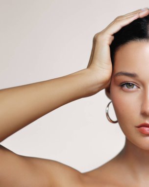 Stüdyoda eli başının üstünde poz veren doğal makyajlı zarif bir kadın. Yarım surat. Güzellik, cilt bakımı ve kozmetik promosyonları için idealdir. Bu yüksek kaliteli görüntü yüz görüntülerini yakalar.