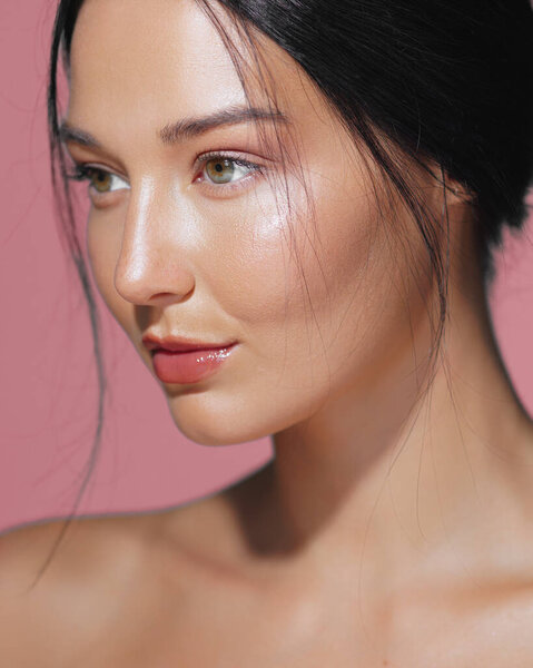 Close-up portrait of a woman with a perfect, hydrated face set against a pink background. Ideal for cosmetics, skincare concepts, beauty advertisements, and high-quality promotional materials.