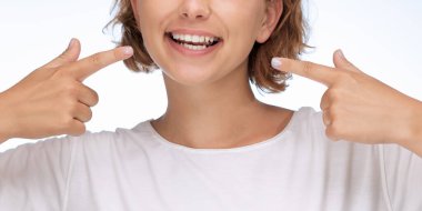 Dişlerini gösteren mutlu bir kadının yakın plan görüntüsü beyaz bir arka planda, diş sağlığı, pozitiflik ve kendine güveni simgeleyen bir gülümsemeyle. Diş reklamları ve ağız temizliği kampanyaları için mükemmel.