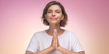 Beyaz gömlekli bir kadın, Namaste jesti ile farklı bir arkaplana karşı farkındalık uygular. Bu kaliteli stok fotoğrafı huzuru ve iç huzuru yakalar, sağlık ve meditasyon için mükemmeldir.