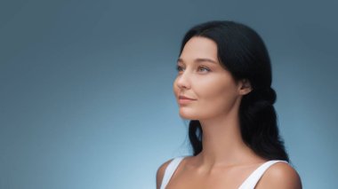 Uzun siyah saçları ve pürüzsüz derisi olan zarif bir Asyalı kadın mavi arka planda zarifçe poz veriyor. Güzellik, cilt bakımı ve moda reklamları için ideal, doğal zarafetin altını çizmek ve...