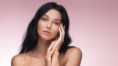 Uzun siyah saçlı zarif bir kadın yumuşak pembe bir arka plana zarif bir şekilde poz verir. Onun dingin ifadesi ve doğal güzelliği bu kaliteli fotoğrafı güzellik, cilt bakımı ve...