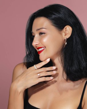 Kırmızı dudaklı, gülümseyen bir kadının zarif portresi pembe arka planda lüks mücevherler sergiliyor. Güzellik, moda ve mücevher promosyonları, yüksek kaliteli reklamlar ve yazı işleri için ideal.