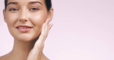 Yüzüne hafifçe dokunan, gülümseyen, parlak tenli, güzel, beyaz bir kadının yakın çekimi. Güzellik, cilt bakımı ve refah kavramları için idealdir. Yüksek kalite resim promosyon kullanımı için mükemmel. 