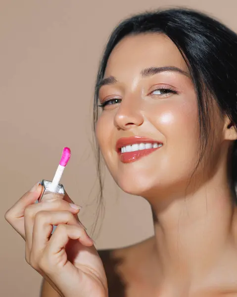 stock image Smiling young woman applying pink lip gloss in a close-up beauty portrait. Perfect for cosmetics, beauty products, and skincare advertisements, showcasing freshness and elegance.