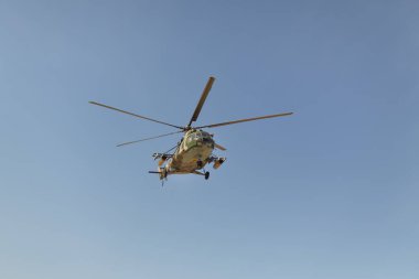 Bir askeri helikopter açık mavi gökyüzüne doğru uçar ve etkileyici tasarımını ve işlevselliğini gösterir. Savunma, havacılık ve askeri konsept promosyonları için mükemmel.. 
