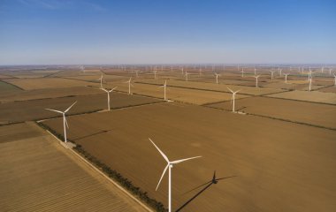 Tarımsal alanlara yayılmış sayısız rüzgar türbini bulunan geniş bir rüzgar çiftliğinin hava görüntüsü kırsal alanda yenilenebilir enerji gösteriyor..