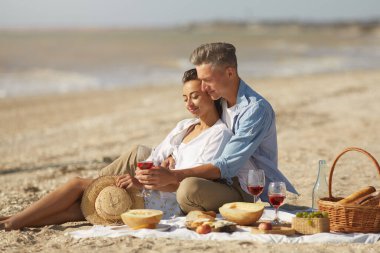 Kumsalda şarap ve yemekle romantik piknik yapan bir çift güneşli bir günde deniz kenarında sevgi dolu bir anı paylaşıyor..