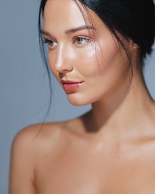 Mavi arka planda poz veren nemli derili zarif bir kadının portresi. Güzellik, cilt bakımı ve kozmetik konsepti reklamları ve yüksek kaliteli promosyon malzemeleri için ideal.