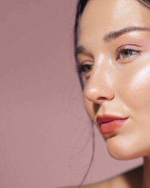 Pembe arka planda parıldayan ciltli ve doğal makyajlı bir kadının yakın plan portresi. Güzellik, cilt bakımı ve makyaj konsepti reklamları ve promosyon malzemeleri için mükemmel..