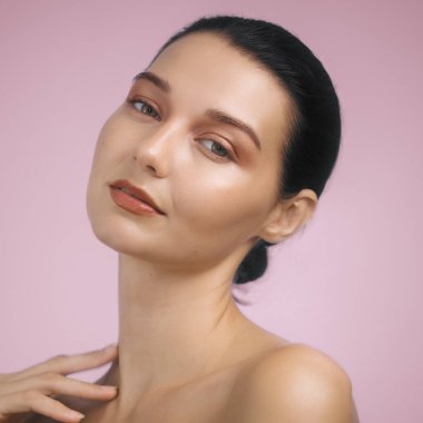 Göz kamaştırıcı esmer kadın, parlak akşam makyajıyla, zarif bir şekilde pembe arka planda poz veriyor. Yüksek kaliteli kampanyalarda güzellik, cilt bakımı ve makyaj ürünleri için ideal..