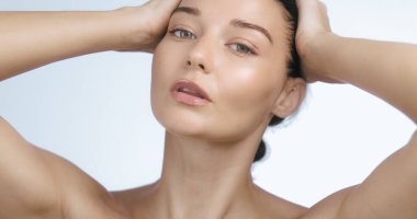 Kendine güvenen bir kadının portresi. Çıplak omuzları ve elleri saçlarında. Parlak bir cilt ve sakin bir ifade. Güzellik kampanyaları, cilt bakımı reklamları ve sağlık promosyonları için mükemmel..