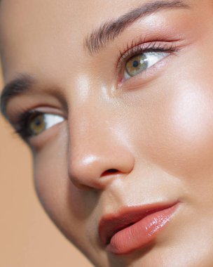 Doğal makyajlı ve parlak tenli bir kadının yakın plan fotoğrafı. Bu kaliteli stüdyo görüntüsü yüz bakımı ürünleri, nemlendirici kremler ve cilt bakımları için mükemmeldir..