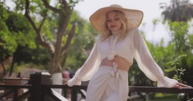 Beyaz elbiseli ve güneş şapkalı şık bir kadının açık havada güneşli bir günün keyfini sürerken çekilmiş yavaş çekim görüntüleri. Moda promosyonları, yaşam tarzı blogları ve seyahat içeriği için mükemmel..
