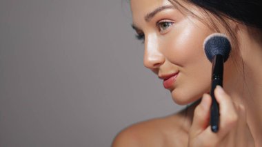 Güzel bir kadının profil fırçasıyla makyaj yaptığı göz kamaştırıcı bir yakın çekim. Güzellik, cilt bakımı ve kozmetik kavramlar için mükemmel. Promosyon malzemeleri ve reklamlar için ideal..