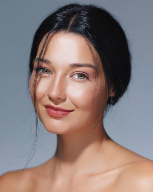 Gülümseyen bir kadının portresi. Parlak, nemli bir teni ve mavi bir arka planı olan doğal bir güzelliği var. Güzellik, cilt bakımı ve kozmetik reklamları ve yüksek kaliteli promosyon malzemeleri için ideal.