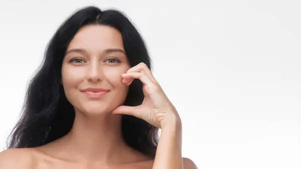 stock image A smiling Asian woman with flawless skin making a half-heart gesture with her hand against a white background. Perfect for themes of beauty, love, and skincare, ideal for cosmetics and lifestyle