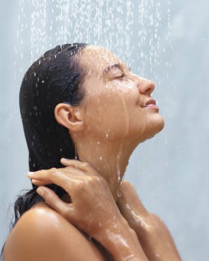 Gözleri kapalı, duşun ferahlatıcı suyunun tadını çıkaran sakin bir kadının yakın çekimi. Elleri nazikçe boynunda duruyor. Huzur ve öz-bakım anı yakalıyor. Terfi için ideal