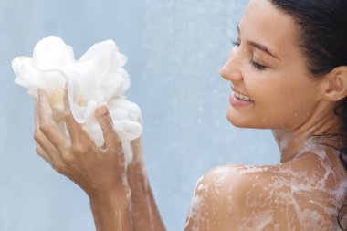 Bir kadın rahatlatıcı bir duş sırasında köpüklü bir banyo lifiyle yıkanmaktan zevk alırken gülümser. Özbakımın ve temizliğin özünü yakalıyor. Güzellik, cilt bakımı ve cilt bakımı için mükemmel.