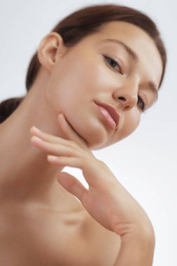 Kusursuz derisi olan genç bir kadının yakın plan portresi, rahat bir şekilde çenesine dokunuyor. Güzellik, cilt bakımı ve sağlık kampanyaları için mükemmel. Kozmetik ve kişisel için yüksek kaliteli görüntü
