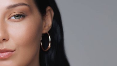 Kusursuz cildine ve zarif halka küpelerine odaklanan bir kadının yüzünün yakın çekimi, minimalist ve zarif bir portrede yer alıyor. Güzellik, moda ve cilt bakımı için ideal.