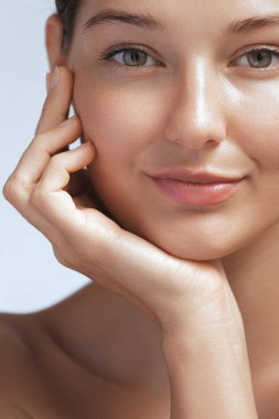 Pürüzsüz tenli bir kadının yakın plan portresi. Elini nazikçe yüzüne koyuyor. Işıl ışıl cildini ve doğal güzelliğini vurguluyor. Cilt bakımı, güzellik ve sağlık promosyonları için ideal.. 