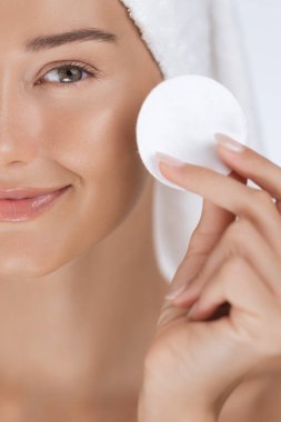 Yüzüne havlu sarılmış gülümseyen bir kadının yüzünün yarısı. Yüzüne pamuk tutuyordu. Cilt bakımına hazırdı. Güzelliği, özgüveni ve refahı göstermek için mükemmel.