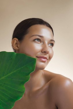 A beautiful woman with glowing, radiant skin holds a large green leaf, symbolizing natural and eco-friendly skincare. Perfect for promoting organic beauty, wellness, and nature-inspired skincare clipart