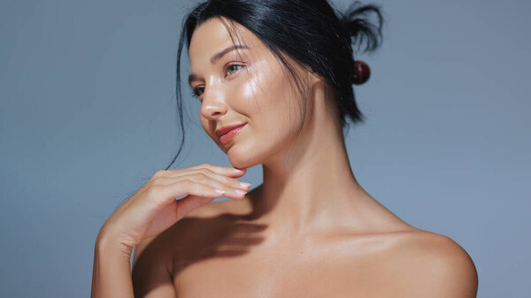 Элегантная женщина с натуральным макияжем и сияющей кожей позирует в студии на синем фоне. Перфект для продвижения красоты, скинкара и косметики, это высококачественное изображение имеет достаточное количество копий