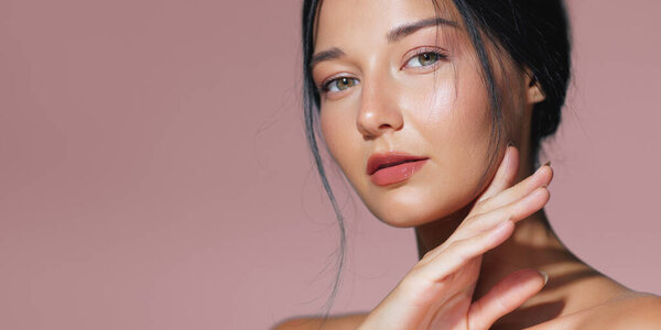 Элегантная женщина с натуральным макияжем изящно позирует на розовом фоне. Перфект для красоты, скинкаре и косметики, это высококачественное изображение имеет достаточно места для копирования для