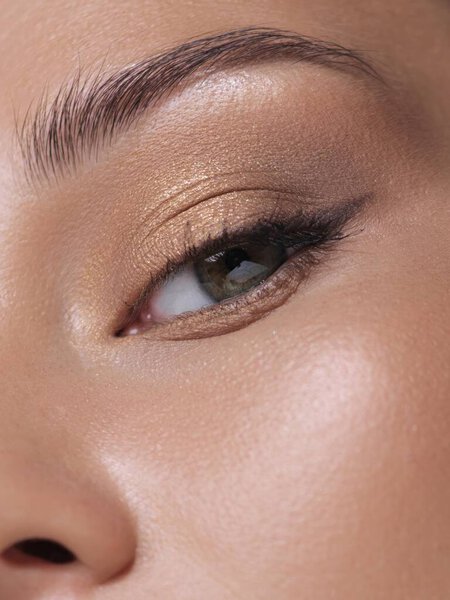 Extreme close-up of a womans eye with flawless skin and subtle gold eyesshadow, emphasizing natural beauty and makeup detail. Идеально подходит для кампаний красоты, косметической рекламы и скинкэр-акций, ориентированных