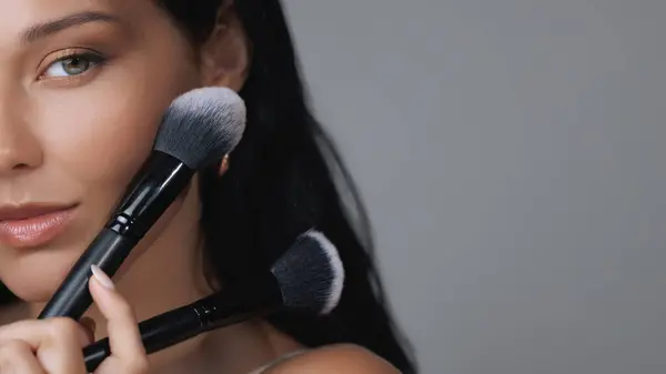 stock image Close-up shot of a woman holding two makeup brushes near her face, symbolizing beauty and skincare routines. Perfect for cosmetic brands, beauty tutorials, or product advertisements, highlighting