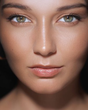 Parlak ciltli ve kusursuz çıplak makyajlı beyaz bir kadının büyüleyici yakın çekimi. Onun delici yeşil gözleri ve parlak dudakları çarpıcı, doğal bir güzellik yaratıyor. Cilt bakımı veya kozmetik için ideal