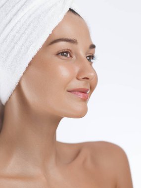 Parlak tenli ve başının etrafına bir havlu sarılmış dingin genç bir kadın. Cilt bakımı, güzellik ya da spa ile ilgili kavramlar için mükemmel. Temiz ve asgari arkaplan doğal güzelliğini vurguluyor..