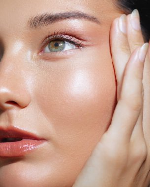 Yüzüne dokunan, parlak bir cilt ve yeşil bir göz gösteren bir kadının yakın çekimi. Cilt bakımı ve güzellik promosyonları, yüksek kaliteli reklamlar ve kavramsal güzellik görselleri için mükemmel..