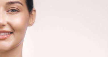 Açık arkaplanda geniş bir kopya alanı olan, ışıl ışıl cildi gülümseyen beyaz bir kadının yarım yüzü. Güzellik, cilt bakımı ve sağlık konuları için mükemmel. Yüksek kaliteli resim ideali