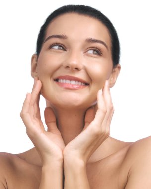 Beyaz bir arkaplana hafifçe dokunan elleri ile gülümseyen, ışıl ışıl, genç, beyaz bir kadının yakın çekimi. Cilt bakımı, güzellik ve sağlık konuları için mükemmel. Yüksek kaliteli resim için ideal