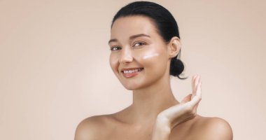 Yanağına cilt kremi sürerken gülümseyen, doğal makyajlı, ışıl ışıl beyaz bir kadının yakın çekimi. Güzellik, cilt bakımı ve sağlık reklamları için mükemmel. Yüksek çözünürlüklü resim uygun
