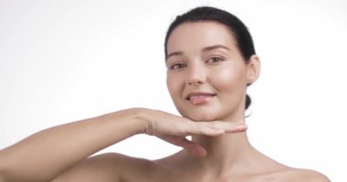 Parlak cildi olan genç bir kadın elleriyle yüzünü çerçevelerken usulca gülümsüyor ve doğal güzelliğini sergiliyor. Minimalist arka plan ve zarif poz bu görüntüyü cilt bakımı ve güzellik için mükemmel yapar.