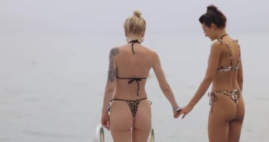 Bikinili bir LGBTQ çifti Mısır 'ın Sharm El Sheikh şehrinde yüzen bir iskeleye el ele tutuşmuş, Kızıl Deniz' de yüzmeye hazırlar. Seyahat reklamları, LGBTQ içeriği ve yaz tatili promosyonları için mükemmel..