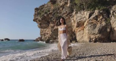 Tarz sahibi bir kadın, Türkiye 'nin Antalya kentinde bir çakıl taşı plajında şık bir yaz kıyafeti içinde geziniyor. Bu görüntü, şık bir sahil kaçamağının özünü yansıtıyor. Seyahat ve tatil için ideal.