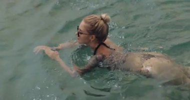 Bikinili iki kadın güneşli bir günün tadını çıkararak denizde birlikte yüzüyor. Yaz tatili promosyonları, yaşam tarzı reklamları ve plaj temalı videolar için mükemmel..