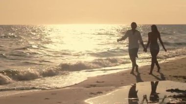 Romantik bir çift kumsalda gün batımı yürüyüşünden zevk alır, el ele tutuşup kucaklaşırlar. Altın saat ışığı huzurlu ve samimi bir atmosfer yaratır. Romantik bir akşam için mükemmel..