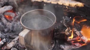 Parlayan közler ve yanmış odunlarla çevrili bir kamp ateşinin üzerinde kaynayan metal bardak açık hava yemek ve maceranın özünü yakalıyor. Kamp, hayatta kalma ve vahşi doğa kavramları için idealdir.. 
