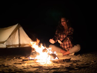 Açık havada giyinmiş bir kadın, geceleri çöldeki bir çadırın yanında sıcak bir kamp ateşi yakmaktan hoşlanır. Kamp, macera, açık hava aktiviteleri ve rahatlama kavramları için mükemmel..